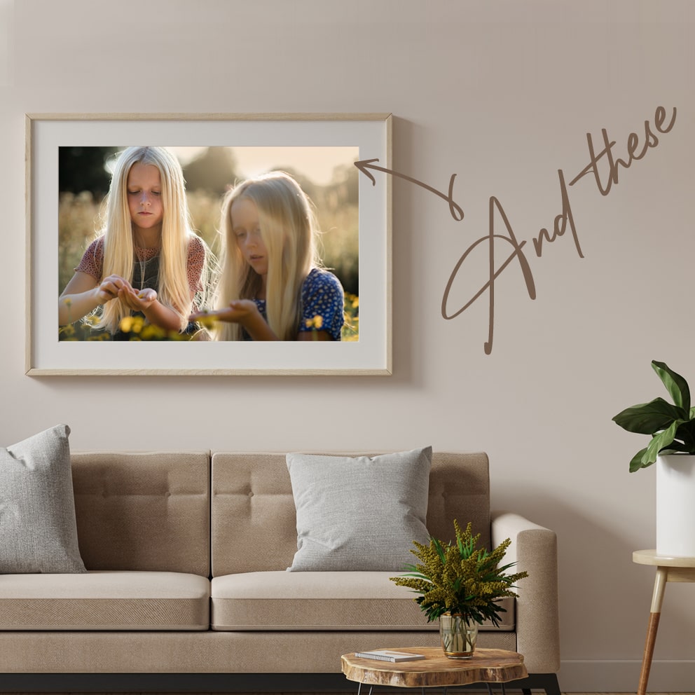 A large framed photo of two children playing in a field, taken by professional photographer Emma Seaney. Shown hanging on a living room wall.